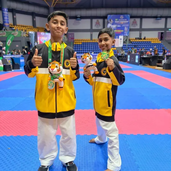 Two Perak Legends students in yellow and black jackets giving a thumbs up with their medals